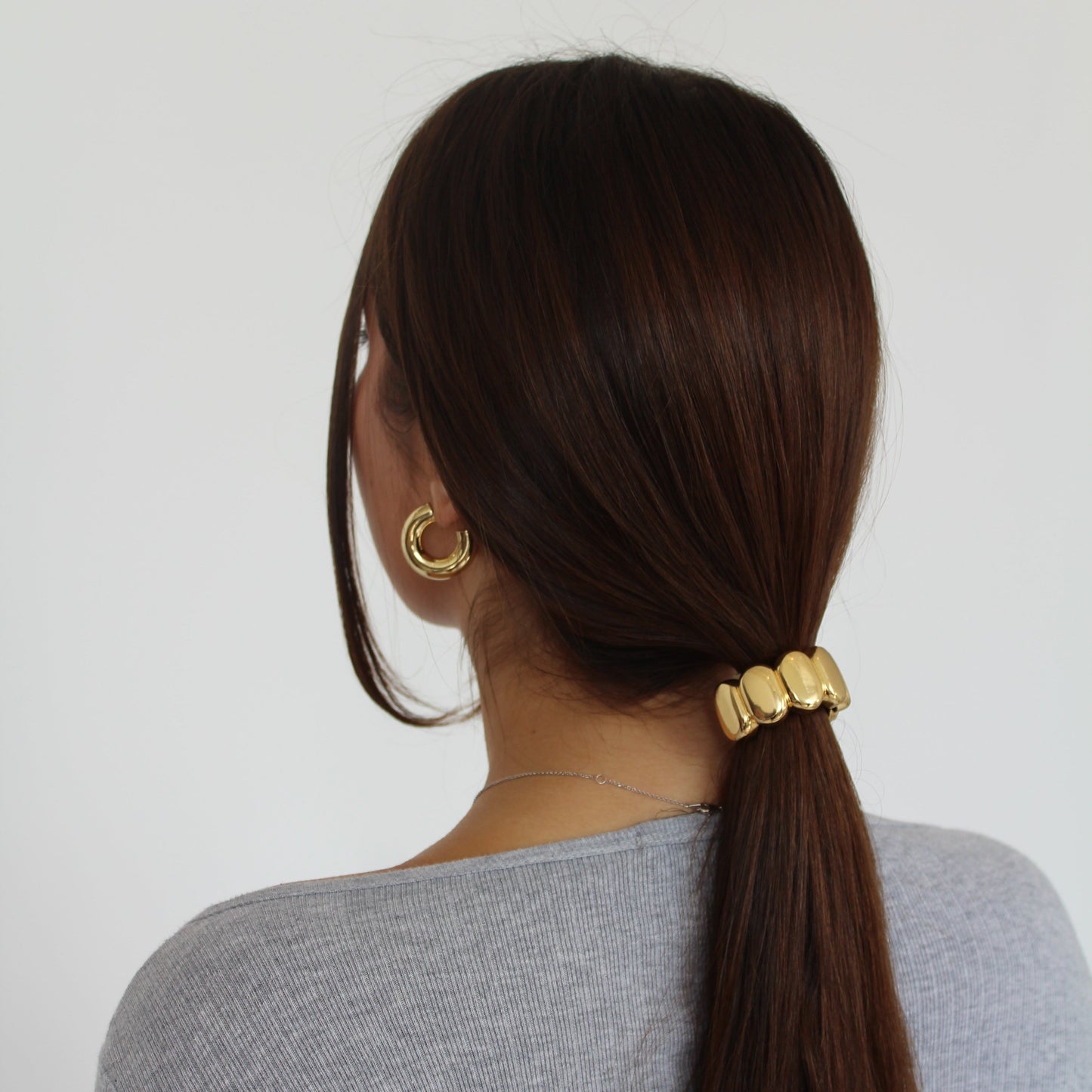 Women with long brown hair wearing a gold ponytail cuff and gold earrings