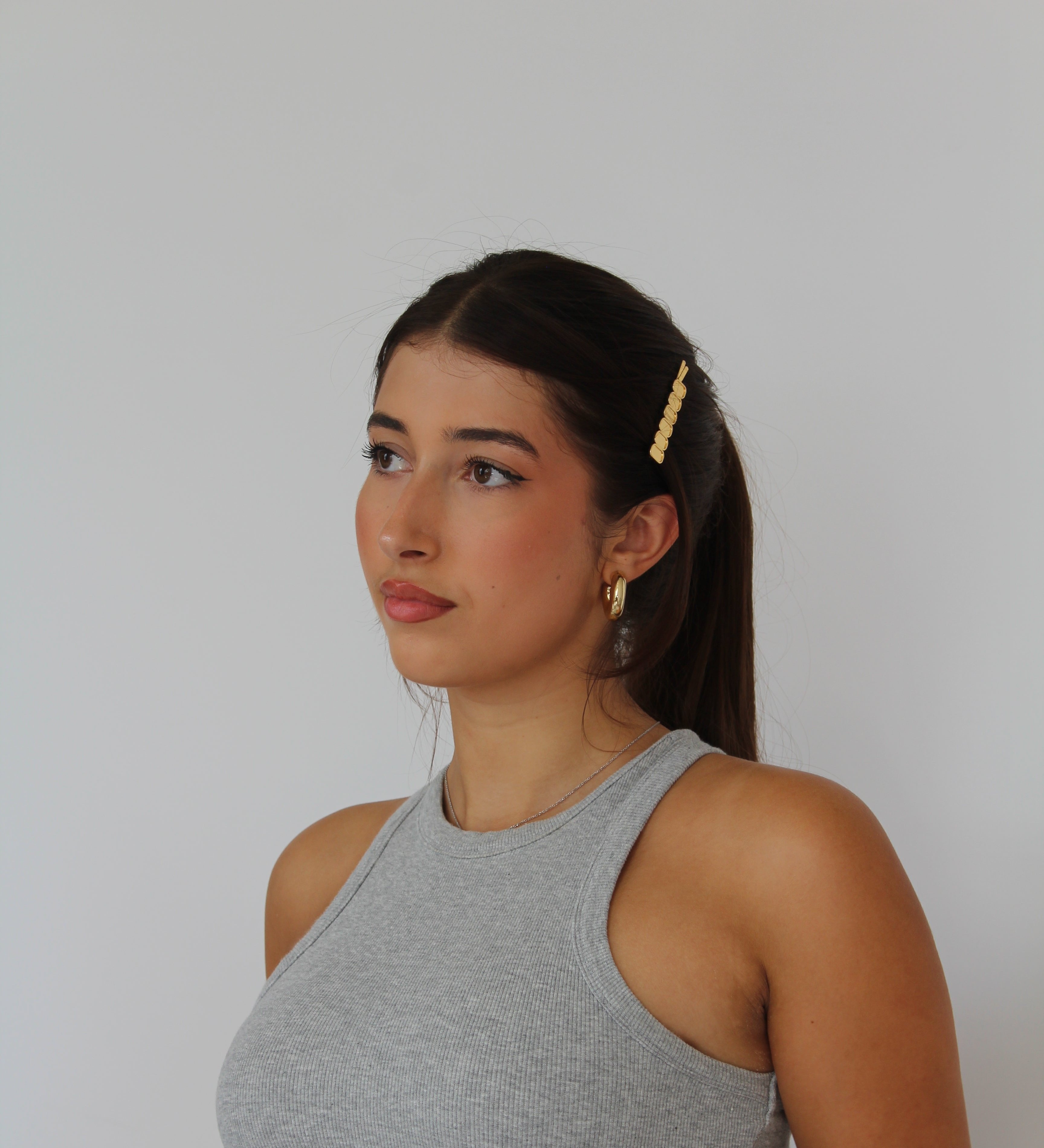 Women with long brown hair in a ponytail, wearing gold hairpin and grey tank top