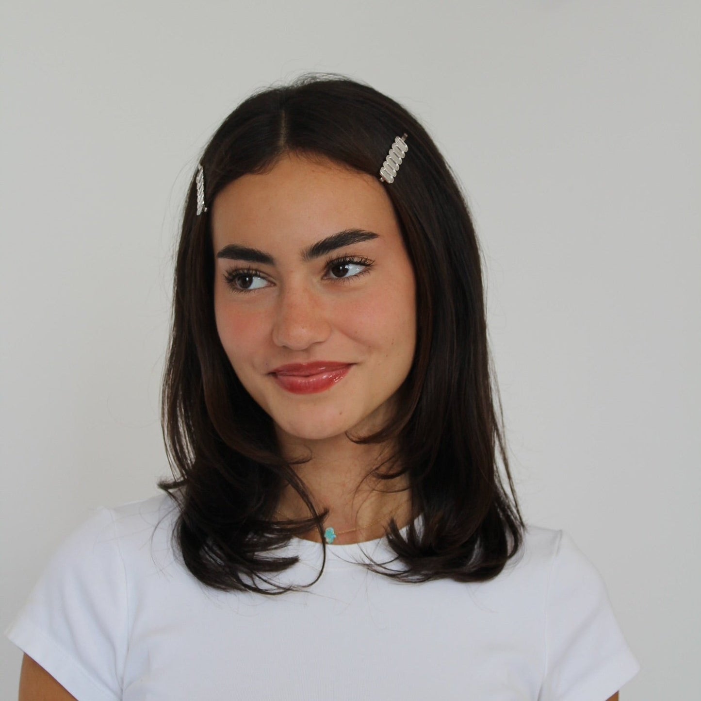 Women with brown hair wearing silver metal hairpins, dressed in a white t-shirt