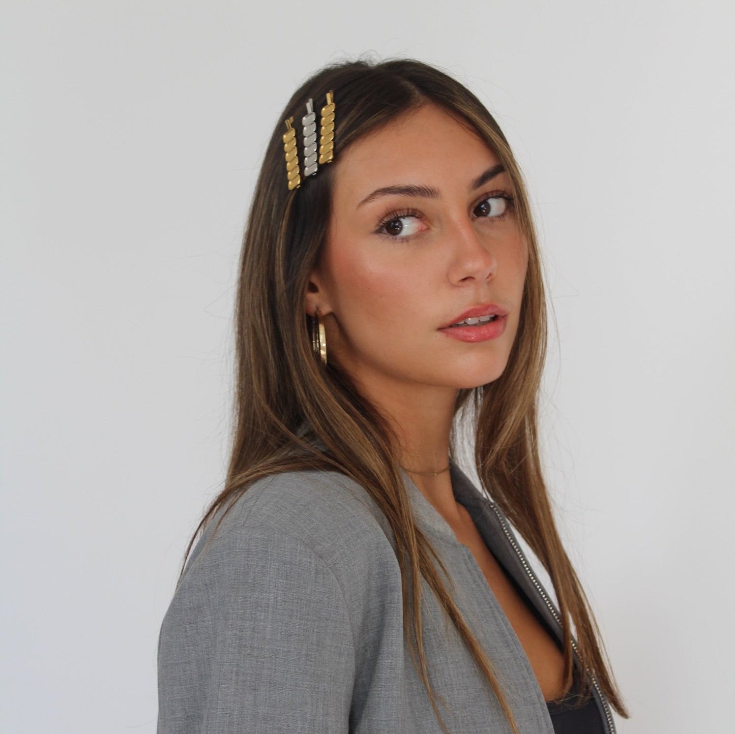 Women with brown hair wearing silver and gold hairpins, dressed in grey blazer